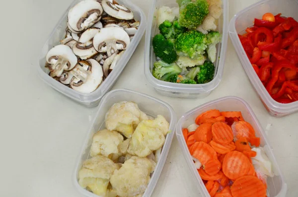 Δίσκοι με ωμά λαχανικά για κατάψυξη. Αποθηκεύοντας για χειμερινή αποθήκευση σε πλαστικά δοχεία, βάζει σε ένα κουτί για να παγώσει κόκκινες πιπεριές, μπρόκολο, κουνουπίδι, καρότα — Φωτογραφία Αρχείου