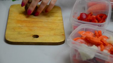 Aşçının elleri ahşap masaya kırmızı dolma biber koyarak dondurucu bir kutuya koyar.