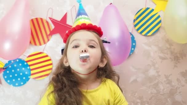 Retrato de una niña bonita con pastel de cumpleaños. una chica en una gorra celebra su cumpleaños, se divierte, sopla una pipa, sopla las velas en el pastel, come un pastel, bebe jugo, lleva una máscara durante un — Vídeos de Stock