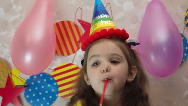 Retrato de una niña bonita con pastel de cumpleaños. una chica en una gorra celebra su cumpleaños, se divierte, sopla una pipa, sopla las velas en el pastel, come un pastel, bebe jugo, lleva una máscara durante un — Vídeos de Stock