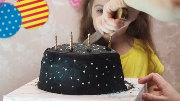 Portré egy csinos kislányról szülinapi tortával. Egy sapkás lány megünnepli a születésnapját, jól érzi magát, pipát fúj, elfújja a gyertyákat a tortán, tortát eszik, gyümölcslevet iszik, maszkot visel a — Stock videók