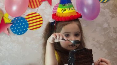 Doğum günü pastası ile küçük güzel bir kızın portresi. Şapkalı bir kız doğum gününü kutlar, eğlenir, pipo üfler, pastadaki mumları söndürür, pasta yer, meyve suyu içer, maske takar.