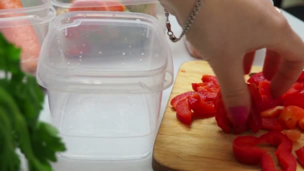 La muchacha corta hortalizas congelar, los ponen en el congelador para el almacenaje. Diferentes verduras congeladas en un plato blanco entre varias verduras frescas parcialmente deslizadas en la tabla de cortar en una mesa de cocina — Vídeo de stock