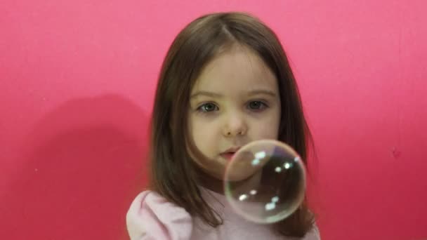 Niña linda sopla y atrapa burbujas de jabón brillante, un niño en una naturaleza de estudio de fondo rosa, juegos activos, recreación y turismo. — Vídeos de Stock