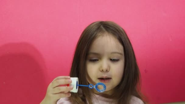 Piccola ragazza carina soffia e cattura bolle di sapone luminose, un bambino su uno sfondo rosa studio natura, giochi attivi, ricreazione e turismo. — Video Stock