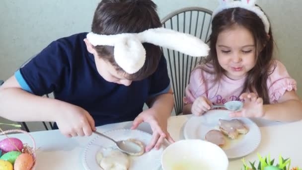 Junge und Mädchen bereiten lachend Plätzchen für Ostern vor. Spaß bei der Ostereiersuche. Junge und Mädchen tragen Hasenohren und bemalen Eier. bunte Eier. — Stockvideo