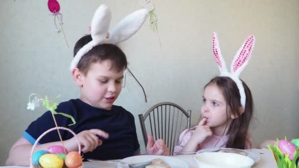 Chico y chica están preparando galletas para la Pascua, riendo. Divertirse en la búsqueda de huevos de Pascua. Niño y niña usando orejas de conejo y pintando huevos. huevos coloridos. — Vídeo de stock