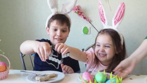 Chico y chica están preparando galletas para la Pascua, riendo. Divertirse en la búsqueda de huevos de Pascua. Niño y niña usando orejas de conejo y pintando huevos. huevos coloridos. — Vídeos de Stock
