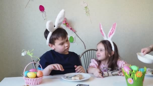 Jongen en meisje bereiden koekjes voor Pasen, lachen. Plezier hebben op de paaseieren jacht. Kind en meisje met konijnenoren en eieren aan. kleurrijke eieren. — Stockvideo