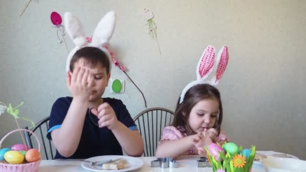 Boy and girl are preparing cookies for easter, laughing. Having fun on Easter egg hunt. Child boy and girl wearing bunny ears and painting eggs. colorful eggs. — Stock Video