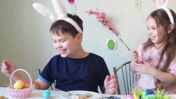 Chico y chica están preparando galletas para la Pascua, riendo. Divertirse en la búsqueda de huevos de Pascua. Niño y niña usando orejas de conejo y pintando huevos. huevos coloridos. — Vídeos de Stock