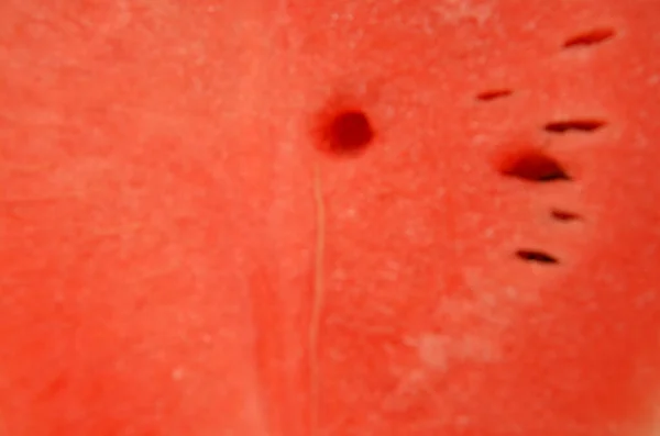 Watermelon put on a chopping block. Hands are holding water melon. A hand holding a knife. Watermelon was cut and separated. Watermelon is red, green, and moist. Water melon looks delicious.