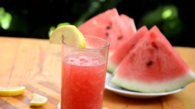 Renkli tropikal taze karpuz smoothie yaz içecekleri ahşap masa arkasındaki bardaklarda. Yeşil yaprakların arka planında sümüklü karpuz pamuğu serinletiyor. Konsept: