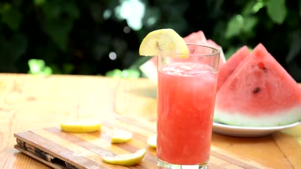 Színes trópusi friss görögdinnye smoothie nyári italok a poharak fa asztal háttér. Frissítő görögdinnye coteil nyálkás háttér zöld lombozat. A következők fogalma: — Stock videók