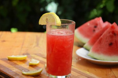 Renkli tropikal taze karpuz smoothie yaz içecekleri ahşap masa arkasındaki bardaklarda. Yeşil yaprakların arka planında sümüklü karpuz pamuğu serinletiyor. Konsept: