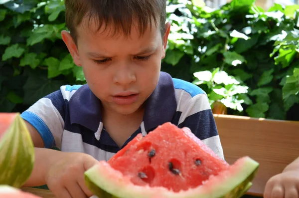 Funny kid eating watermelon outdoors in summer park, focus on eyes. Child, baby, healthy food — Stock Photo, Image