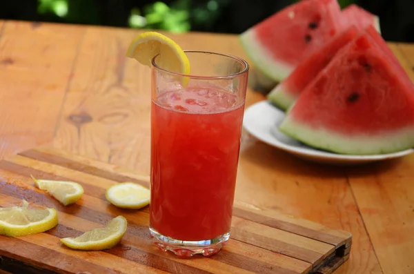 木のテーブルの背景にガラスのカラフルなトロピカルフレッシュスイカスムージー夏の飲み物。緑の葉を背景にスリムで爽やかなスイカのコテイル。概念 — ストック写真