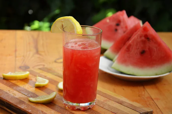 Красочные тропические свежие арбузные коктейли летом напитки в стаканах на деревянном фоне стола. Освежающий арбузный котейль со слимоном на фоне зеленой листвы. Концепция — стоковое фото