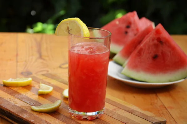 木のテーブルの背景にガラスのカラフルなトロピカルフレッシュスイカスムージー夏の飲み物。緑の葉を背景にスリムで爽やかなスイカのコテイル。概念 — ストック写真