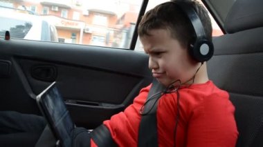 Arabada kemer, koltuk ve tabletle oynayan, kulaklık takan çizgi film izleyen, iletişim kuran mutlu küçük çocuk. Eğlenceli yolculuk.
