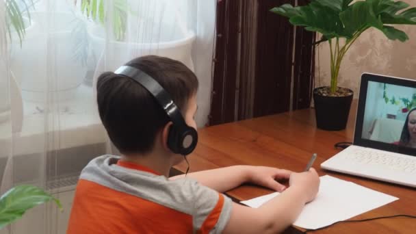 テーブルに座って宿題を書くか、試験の準備をする頭の良い未成年の少年。10代はノートパソコンを使って勉強する。学生、学校、リモート、オンライン学習、新しい通常、ホームベースの学習. — ストック動画