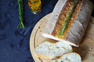 İtalyan ciabatta ekmeği, ahşap kesim tahtasına dilimlenmiş, otlar, sarımsak ve zeytinlerle koyu grunge karşı, üst manzara.