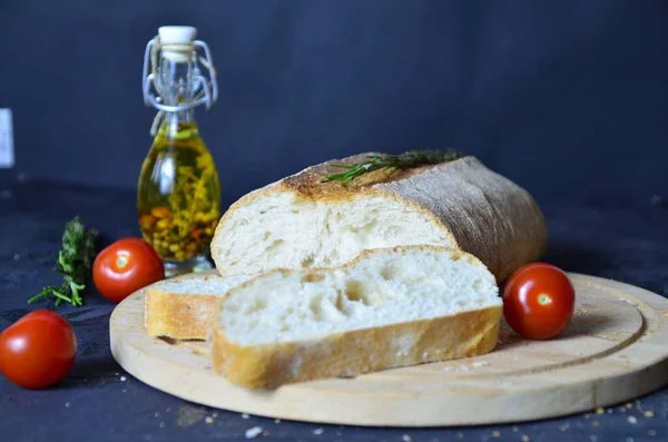 Italienisches Ciabatta-Brot in Scheiben geschnitten auf hölzernem Schneidebrett mit Kräutern, Knoblauch und Oliven vor dunklem Grunge-Hintergrund, Draufsicht — Stockfoto