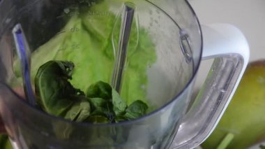 Ispanak, salatalık ve buz karıştıran bir kadın sağlıklı yeşil meyve suyu yapmak için. Kadın blenderdan bardağa yeşil detoks suyu döküyor..