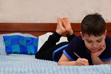 Çocuk evde kanepede ya da yatakta ev işi yapıyor, konuyu okuyor, kitap okuyor ve notlar yazıyor. Çevrimiçi ev eğitimi, oda öğrencileri için çevrimiçi kurslar, dizüstü bilgisayarla çalışmak