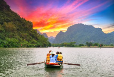Ninh Binh, Vietnam - 5 Nisan 2019 Tam Coc Ulusal Parkın gün batımı gökyüzünde turistleri taşıyan sandallarda kürek çeken adam. Burası Ninh Binh, Vietnam 'da popüler bir turizm beldesi..