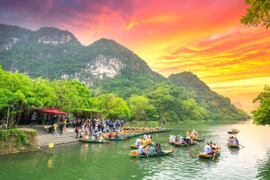 Ninh Binh, Vietnam - 5 Nisan 2019 Tam Coc Ulusal Parkın gün batımı gökyüzünde turistleri taşıyan sandallarda kürek çeken adam. Burası Ninh Binh, Vietnam 'da popüler bir turizm beldesi..