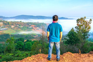 Da Lat, Vietnam - 30 Mart 2021: Vadi sisli dağlarda yüksek bir tepede duran bir adamın silueti Vietnam 'ın başkenti Da Lat' ta dalgalanan büyük bir manzarayı örtüyordu.