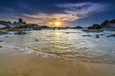 Beautiful sunrise on the beach below the waves lapping at the shore of the soft great to welcome the peaceful new day