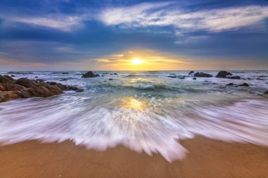 Denizin sahilinde gün doğumu dalgalar ve kayalarla