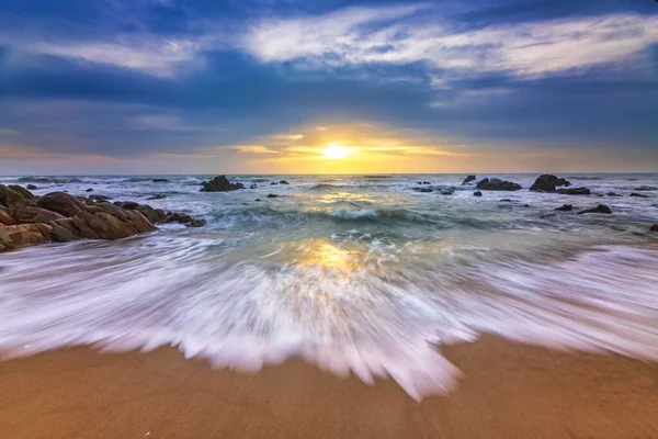 Denizin sahilinde gün doğumu dalgalar ve kayalarla