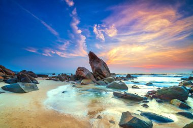 Kumlu bir sahilden yükselen dramatik bir kaya oluşumunun yer aldığı güzel bir sahil gündoğumu sahnesi..