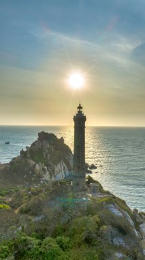 Okyanusa bakan kayalık bir sahil manzarasında duran uzun ve eski bir deniz fenerinin manzarası..