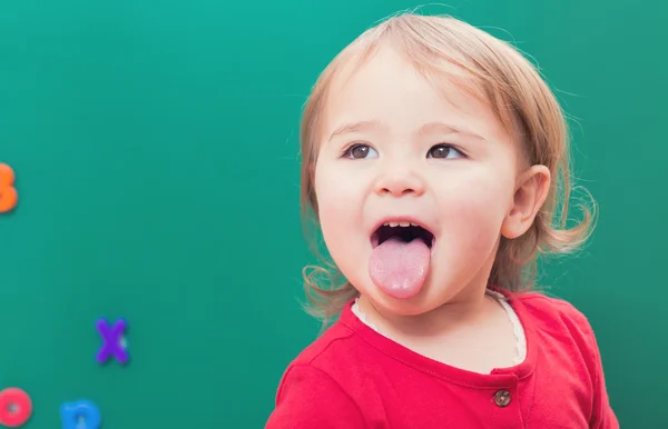 Κορίτσι να κολλήσει τη γλώσσα έξω μπροστά από ένα πίνακα κιμωλίας — Φωτογραφία Αρχείου