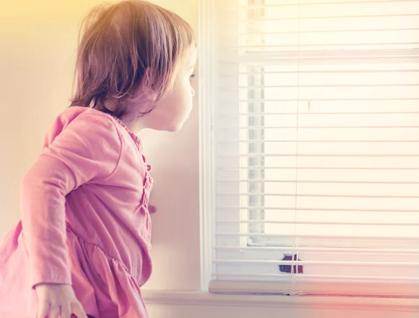 Barn girl kikar ut genom fönstret — Stockfoto