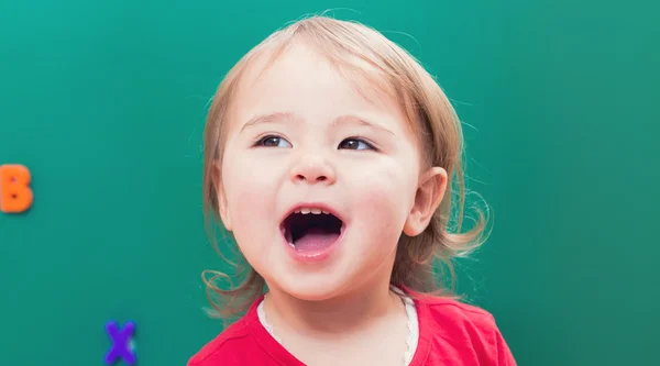 Menina criança sorrindo na frente de um quadro verde — Fotografia de Stock