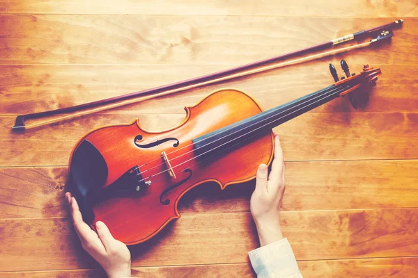 Persona sosteniendo un violín sobre una mesa de madera — Foto de Stock