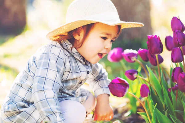 Flicka i en hatt som leker med lila tulpaner — Stockfoto