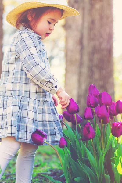 Menina de criança em um chapéu brincando com tulipas — Fotografia de Stock