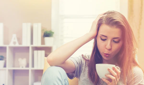 Kvinna som dricker kaffe på hennes soffa — Stockfoto
