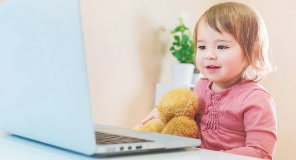 Meisje met behulp van een laptop met haar teddy beer — Stockfoto