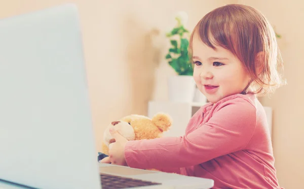 Kleuter meisje met behulp van een laptop met haar teddy beer — Stockfoto