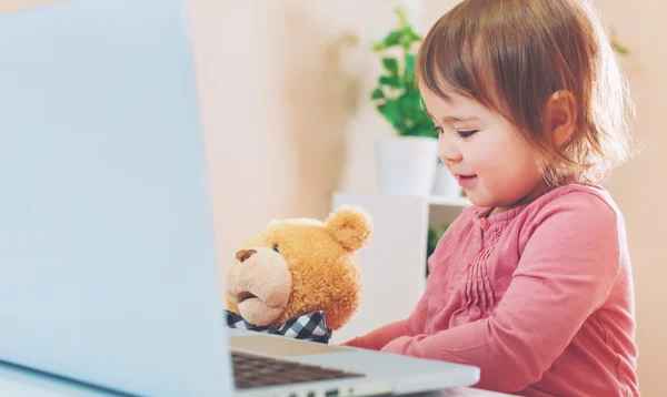 Kleuter meisje met behulp van een laptop met haar teddy beer — Stockfoto