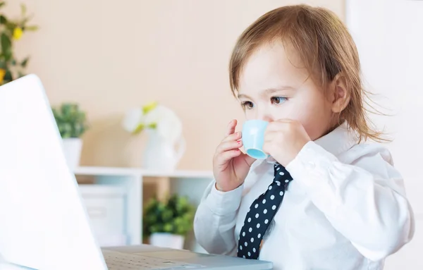 Dziewczyna malucha picia z kubka przed laptopa — Zdjęcie stockowe