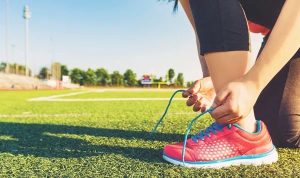 Female jogger tying her shoes on a stadium field — Stock Photo, Image
