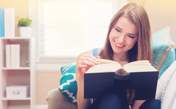 Mulher feliz lendo um livro em seu sofá — Fotografia de Stock